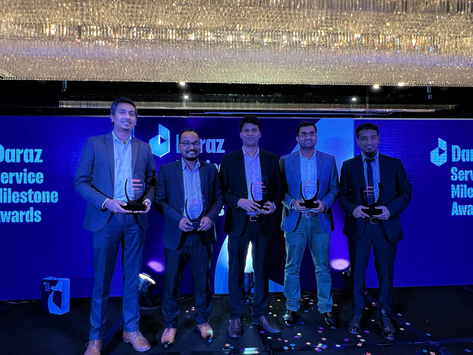 Five Daraz colleagues holding their service milestone trophies in front of the Daraz Service Milestone Awards backdrop