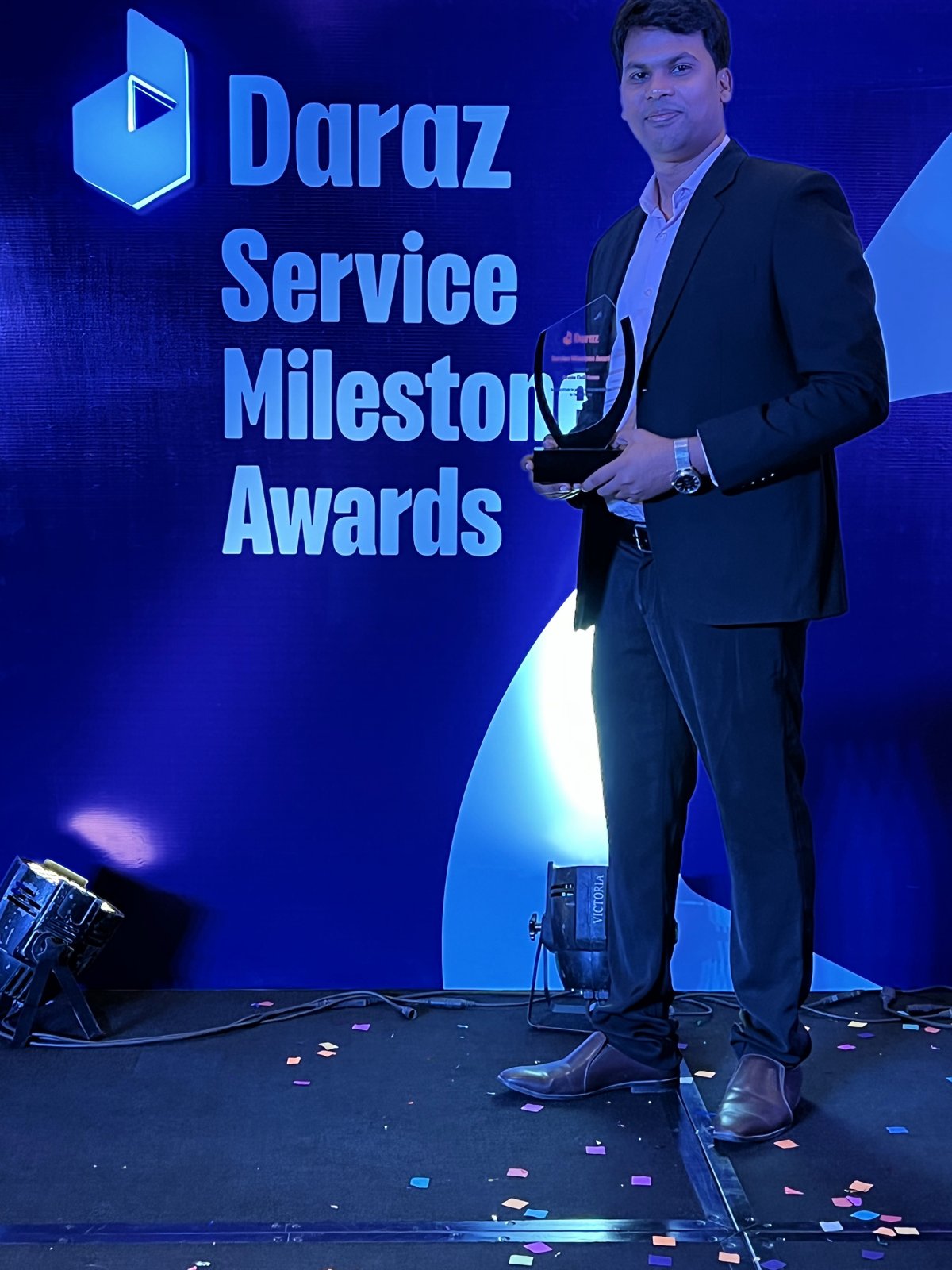 Portrait of an award recipient holding a trophy in front of the Daraz Service Milestone Awards backdrop