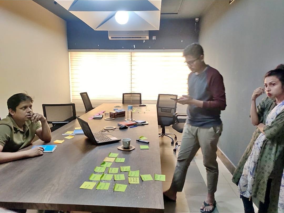 Three people around a table covered in green sticky notes during a research workshop
